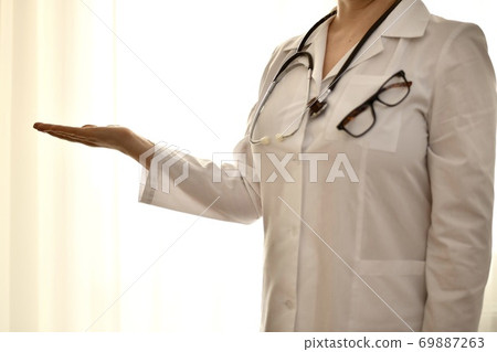 The doctor in a white robe stands with her arm outstretched and an empty palm showing anything.  69887263