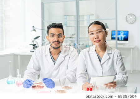 Two young intercultural clinicians in whitecoats looking through online data Two young intercultural clinicians in whitecoats looking through online data 69887604