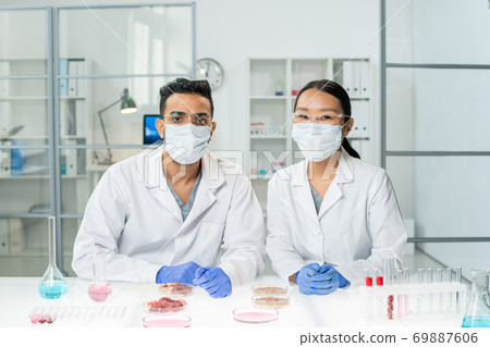 Two young intercultural clinicians in whitecoats, protective masks and gloves 69887606