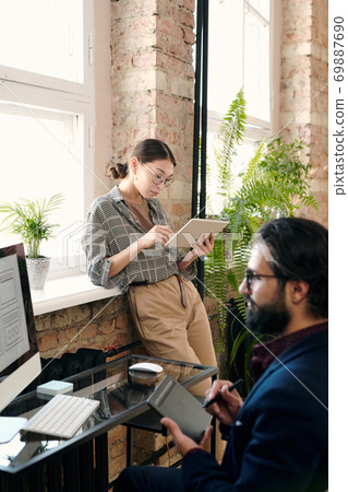 Young female designer using digital tablet while her colleague drawing sketch 69887690