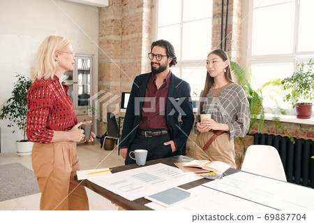 Happy young intercultural colleagues in formalwear looking at mature female Happy young intercultural colleagues in formalwear looking at mature female 69887704