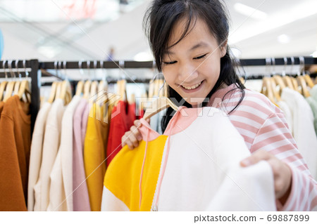 Beautiful asian child girl choosing clothes in shopping center,happy smiling woman customer buying new fashion long sleeved t-shirts during discounted products for herself as a gift in the mall 69887899