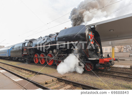 Steam engine. Vintage steam engine at railway station. Black smoke rises from the chimney. 69888843