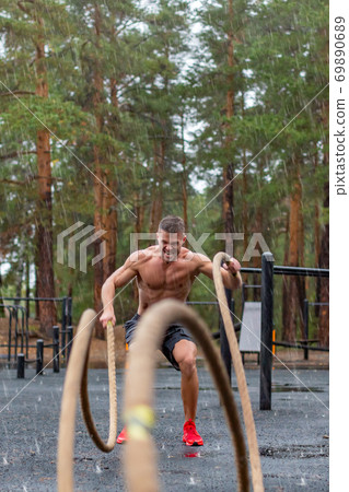Vertical photo of a man having hard workout with a ropes outdoor in a rainy day. 69890689