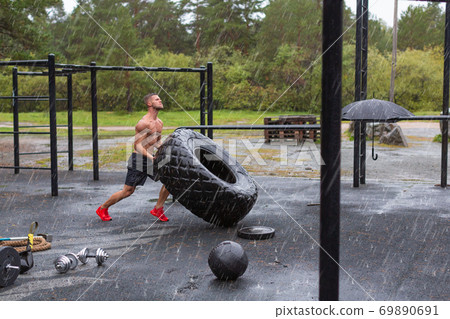 Man flipping a tire. Hard workout on a rainy day. Full length. 69890691