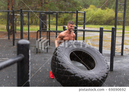 Man flipping a tire. Outdoor workout on a rainy day. Man flipping a tire. Outdoor workout on a rainy day. 69890692