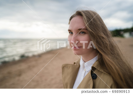 pretty girl walking on a beach in beige trench coat 69890913