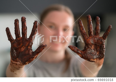Cheerful girl showing her hands covered with chocolate after making candies 69891018