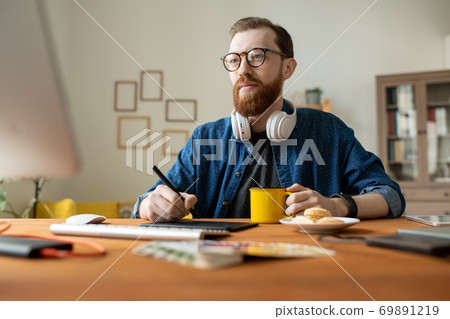 Young creative freelance designer having drink while holding stylus over tablet Young creative freelance designer having drink while holding stylus over tablet 69891219