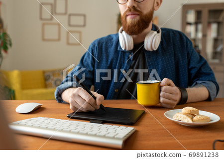Young creative web designer in casualwear having coffee with cookies and drawing Young creative web designer in casualwear having coffee with cookies and drawing 69891238