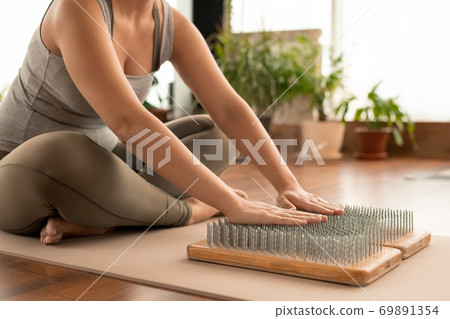 Arms of cross-legged female in activewear sitting on mat in front of yoga pads 69891354