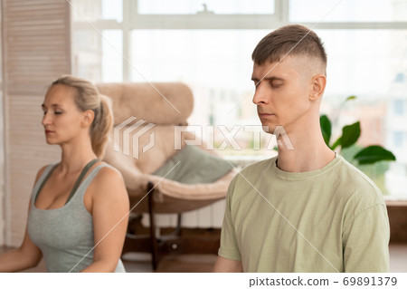 Young relaxed sportsman in activewear keeping eyes closed while meditating Young relaxed sportsman in activewear keeping eyes closed while meditating 69891379
