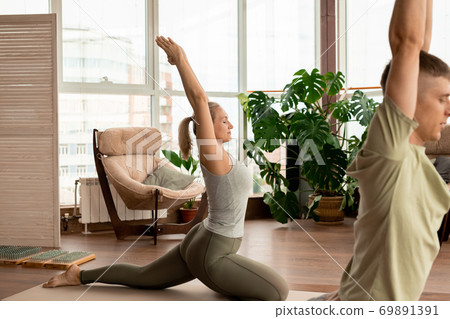 Side view of young active couple in sportswear exercising with raised arms 69891391