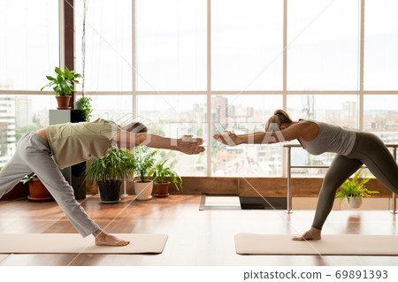 Two young active dates bending forwards while exercising in front of each other Two young active dates bending forwards while exercising in front of each other 69891393