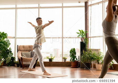 Young active man in sportswear standing on mat with outstretched arms in gym Young active man in sportswear standing on mat with outstretched arms in gym 69891394
