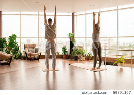Back view of young active couple in sportswear standing on mats with raised arms Back view of young active couple in sportswear standing on mats with raised arms 69891397