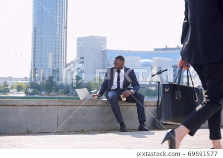 Young elegant businessman with laptop and coffee networking by riverside Young elegant businessman with laptop and coffee networking by riverside 69891577