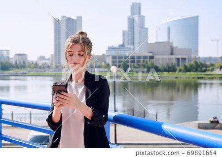 Young contemporary businesswoman in smart casualwear using smartphone Young contemporary businesswoman in smart casualwear using smartphone 69891654