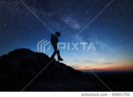Space traveler walking down the rocky hill under starry sky. Space traveler walking down the rocky hill under starry sky. 69891700