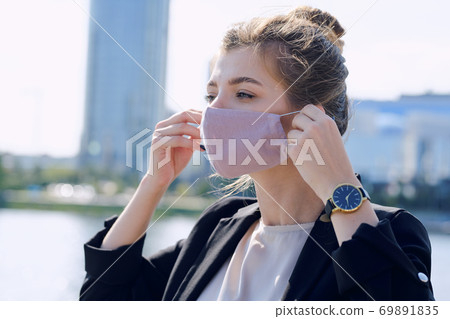 Young elegant businesswoman in formalwear putting on protective mask Young elegant businesswoman in formalwear putting on protective mask 69891835
