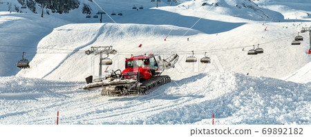 Red modern snowcat ratrack with snowplow snow grooming machine preparing ski slope piste hillalpine skiing winter resort Ischgl in Austria. Heavy machinery mountain equipment track vehicle. panoramic 69892182