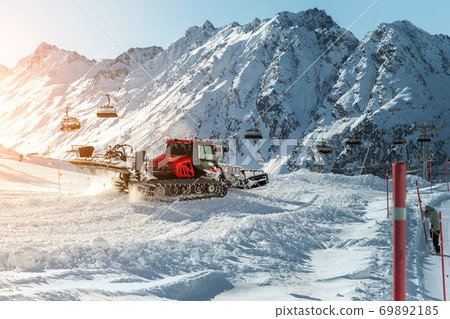 Red modern snowcat ratrack with snowplow snow grooming machine preparing ski slope piste hill at alpine skiing winter resort Ischgl in Austria. Heavy machinery mountain equipment track vehicle 69892185