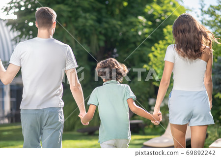 Back view of family of three holding hands, walking in the park Back view of family of three holding hands, walking in the park 69892242