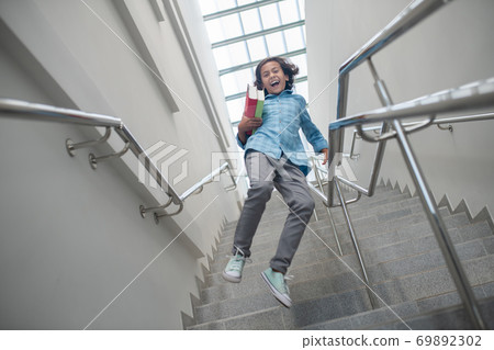 Excited schoolboy running downstairs with pile of books Excited schoolboy running downstairs with pile of books 69892302
