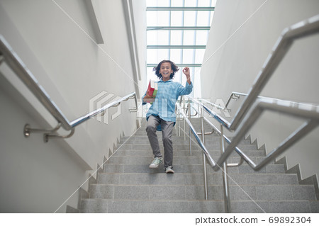 Excited schoolboy running downstairs with pile of books Excited schoolboy running downstairs with pile of books 69892304