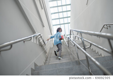 Smiling schoolboy walking upstairs with pile of books Smiling schoolboy walking upstairs with pile of books 69892305