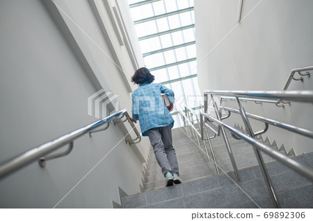 Schoolboy walking upstairs with pile of books Schoolboy walking upstairs with pile of books 69892306