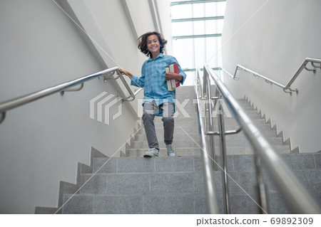 Excited schoolboy holding pile of books, running downstairs Excited schoolboy holding pile of books, running downstairs 69892309