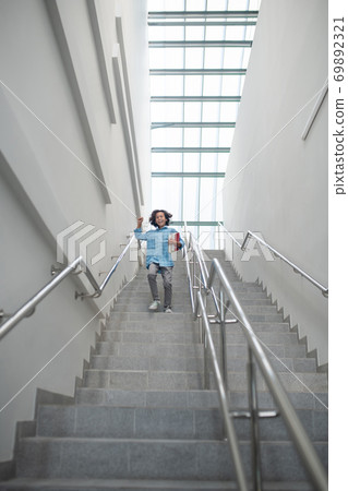 Schoolboy raising his hand, running downstairs with pile of books Schoolboy raising his hand, running downstairs with pile of books 69892321