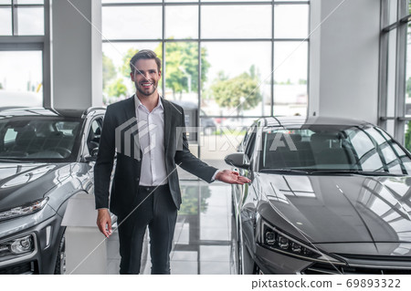 Stylish man in black suit standing near new car and smiling Stylish man in black suit standing near new car and smiling 69893322