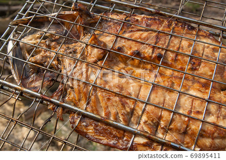Close up view of fresh fish with sauce cooked on an open flame grill.. 69895411
