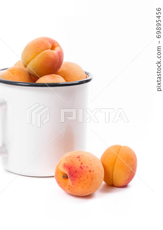 Harvested apricots in white cup with whole and halved apricots on white background.. Harvested apricots in white cup with whole and halved apricots on white background.. 69895456