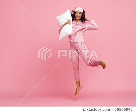 Excited woman in pajama jumping with pillow Excited woman in pajama jumping with pillow 69896945