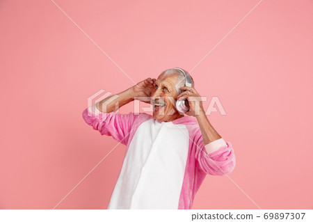 Senior hipster man in stylish pink attire isolated on pink background. Tech and joyful elderly lifestyle concept 69897307