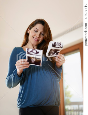 Young Pregnant Woman Comparing Medical Baby Scans Young Pregnant Woman Comparing Medical Baby Scans 69897419