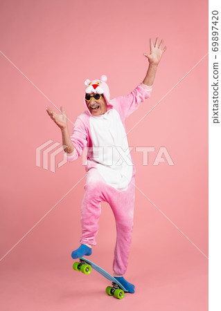 Senior hipster man in stylish pink attire isolated on pink background. Tech and joyful elderly lifestyle concept 69897420