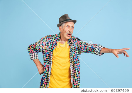 Senior hipster man in stylish hat isolated on blue background. Tech and joyful elderly lifestyle concept Senior hipster man in stylish hat isolated on blue background. Tech and joyful elderly lifestyle concept 69897499