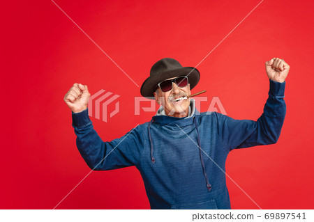 Senior man in stylish eyewear and hat isolated on red background. Tech and joyful elderly lifestyle concept 69897541