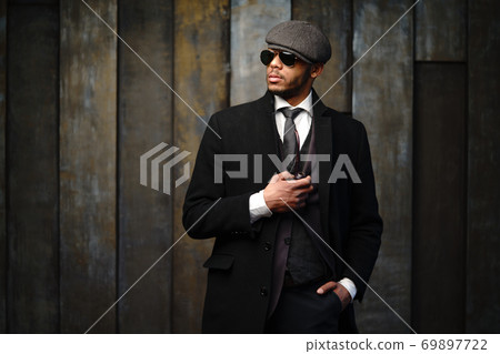 Studio shot of stylish african american man wearing coat, cap, glasses and holding smoking pipe 69897722