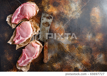 Bunch Pork steaks, fillets for grilling, baking or frying, Pork with ribs. Tenderloin. Entrecote warped in paper with butcher cleaver on side over rustic metall table top view space for text Bunch Pork steaks, fillets for grilling, baking or frying, Pork with ribs. Tenderloin. Entrecote warped in paper with butcher cleaver on side over rustic metall table top view space for text 69897727
