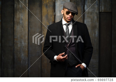Studio shot of stylish african american man wearing coat, cap, glasses and holding smoking pipe 69897728