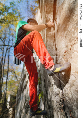 A bearded man at the age of training in free climbing on a rock in the forest against a background of blue sky 69898153