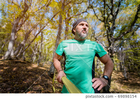 Portrait of an attractive middle-aged man with a beard. Stands in the autumn forest holding on to a taut slackline Portrait of an attractive middle-aged man with a beard. Stands in the autumn forest holding on to a taut slackline 69898154