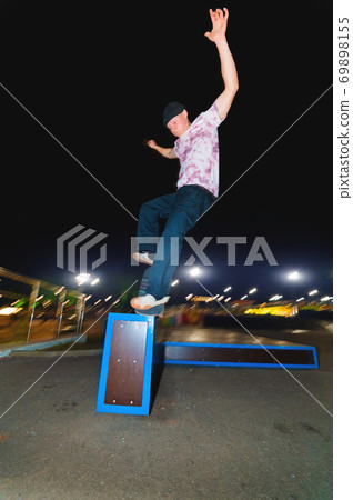 Young skater doing trick slide on railing in skatepark at night 69898155