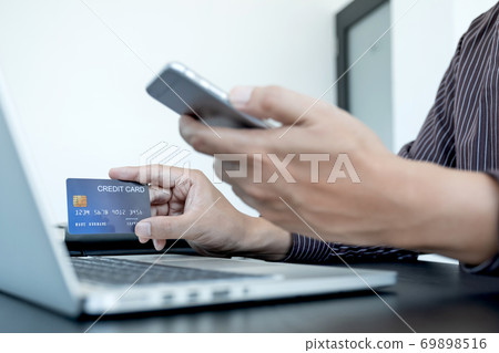 The businessman's hand is holding a credit card and using a smartphone for online shopping and internet payment in the office 69898516