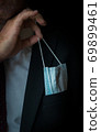 The man takes a disposable medical mask out of his pocket instead of a napkin. A man with a disposable mask in a suit. Respiratory protection. 69899461